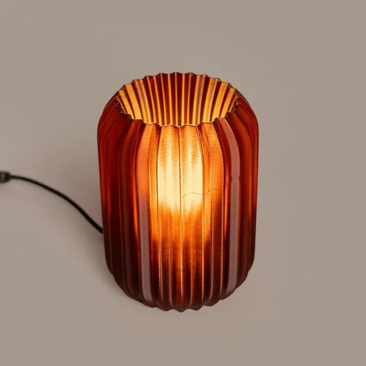 An amber ribbed table lamp, lit, with its cord on the table