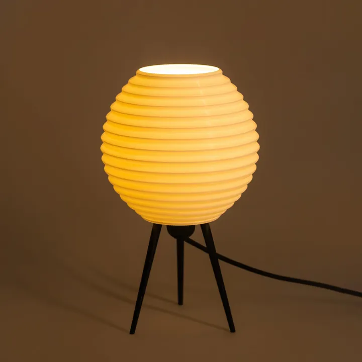 A round shade with horizontal ridges on a black tripod, lit warm yellow